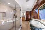 Experience luxury in this spacious bathroom featuring a freestanding soaking tub with a marble surround and a separate glass-enclosed shower with a rainfall showerhead.