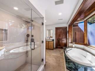 Experience luxury in this spacious bathroom featuring a freestanding soaking tub with a marble surround and a separate glass-enclosed shower with a rainfall showerhead.