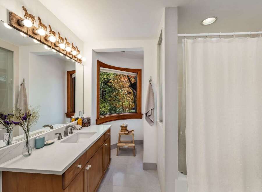 This bathroom features a spacious vanity with a marble countertop and wooden cabinetry, complemented by a unique horse-themed light fixture above the mirror.