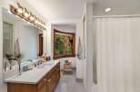 This bathroom features a spacious vanity with a marble countertop and wooden cabinetry, complemented by a unique horse-themed light fixture above the mirror.