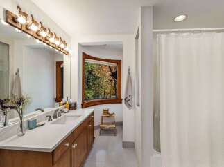 This bathroom features a spacious vanity with a marble countertop and wooden cabinetry, complemented by a unique horse-themed light fixture above the mirror.