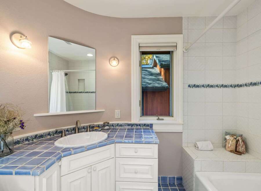 This charming bathroom features a vibrant blue tiled countertop and backsplash, complemented by white cabinetry and a classic white sink.
