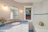 This charming bathroom features a vibrant blue tiled countertop and backsplash, complemented by white cabinetry and a classic white sink.