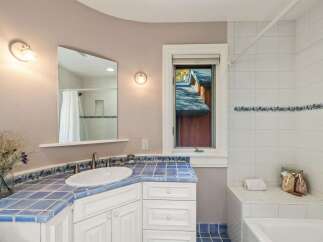 This charming bathroom features a vibrant blue tiled countertop and backsplash, complemented by white cabinetry and a classic white sink.