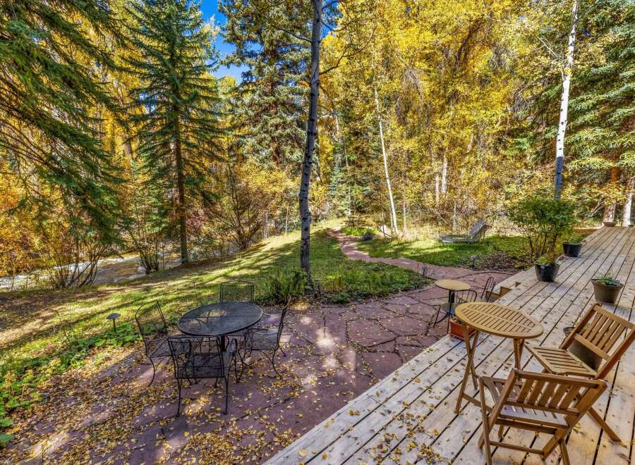 Enjoy the vibrant autumn colors from this charming outdoor living space, featuring a spacious wooden deck and a stone patio perfect for al fresco dining.