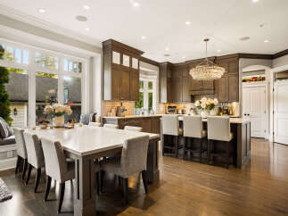 Experience luxury in this stunning kitchen featuring dark wood cabinetry, a large quartz island with bar seating, and a dazzling crystal chandelier.