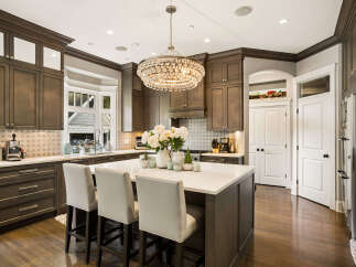 This stunning kitchen boasts dark wood cabinetry, a large marble island with seating, and a dazzling crystal chandelier.