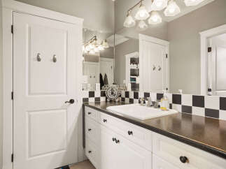 This modern bathroom features a sleek vanity with a dark countertop and white cabinetry, complemented by a crisp black and white checkered backsplash.