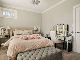 Indulge in luxury with this elegant bedroom featuring a plush tufted ottoman and a mirrored vanity.