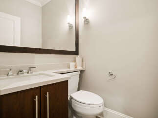 This modern bathroom features a sleek vanity with a marble countertop and dark wood cabinetry, complemented by a matching mirror and elegant sconce lighting.