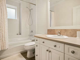 This bright and airy bathroom features a pristine white bathtub with a shower, complemented by a matching toilet and a vanity with ample storage.