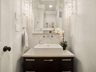 This modern powder room features a sleek white vessel sink atop a dark wood vanity with brushed nickel hardware.