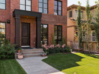 Discover this stunning red brick townhouse featuring a welcoming covered porch with elegant dark pillars and a classic black front door.