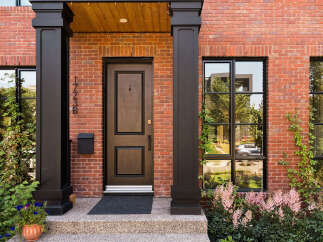 Discover this stunning red brick home featuring a classic dark wood door with elegant trim and a matching mailbox.