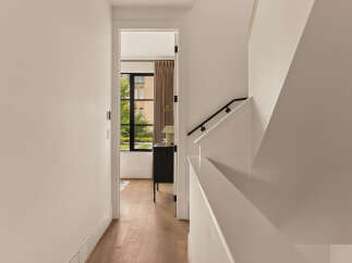 Step into a bright and airy hallway featuring elegant hardwood floors and a modern staircase with a sleek black railing.