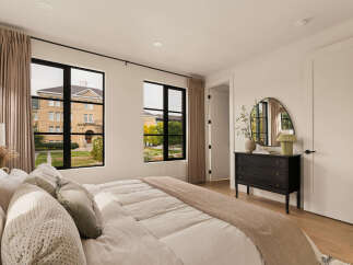 Experience modern comfort in this beautifully appointed bedroom, featuring large black-framed windows that offer picturesque views of the surrounding architecture and greenery.