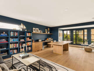 Discover this sophisticated home office featuring a stunning navy blue accent wall, complemented by a spacious wooden desk and extensive built-in bookshelves.