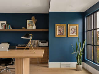 This home office features a large wooden desk with a laptop and a stylish desk lamp, complemented by a wall of dark blue paint.