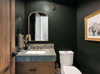 This powder room features a striking dark green accent wall, complemented by a rustic wooden door and vanity.