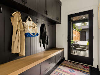 This modern mudroom features a sleek black paneled wall with ample storage, including overhead cabinets and a built-in bench with drawers.