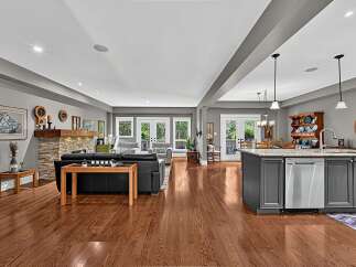 This spacious open-concept living area features a modern kitchen with a large island and stainless steel appliances, seamlessly flowing into a comfortable living room with a stone fireplace.
