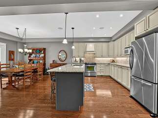 This spacious kitchen and dining area features a large wooden dining table with chairs, a charming hutch filled with decorative plates, and a modern island with granite countertops.