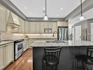 This stunning kitchen boasts elegant cream-colored cabinetry with intricate detailing, complemented by a sleek granite countertop island perfect for entertaining.