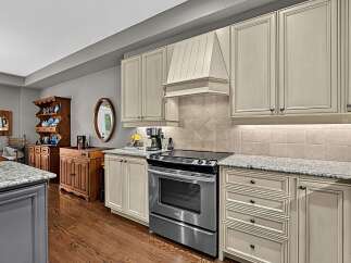 This kitchen boasts elegant cream-colored cabinetry with detailed trim, complemented by a sleek stainless steel range and a granite countertop.
