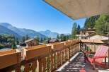 Enjoy breathtaking mountain views from this charming balcony, complete with wooden planters and a comfortable red Adirondack chair.