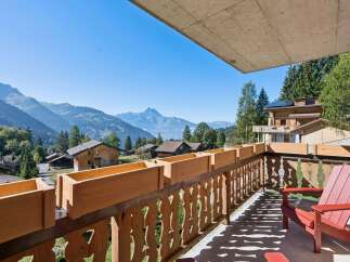 Enjoy breathtaking mountain views from this charming balcony, complete with wooden planters and a comfortable red Adirondack chair.