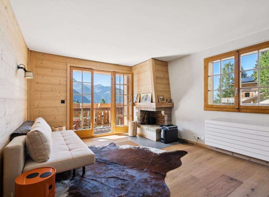 Experience mountain living in this charming living room featuring a cozy fireplace and stunning panoramic views from the balcony.
