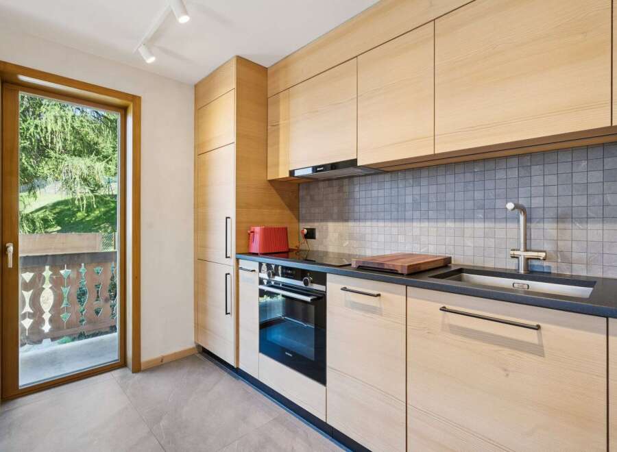Experience modern living in this beautifully appointed kitchen, featuring sleek light wood cabinetry and a stylish grey tiled backsplash.