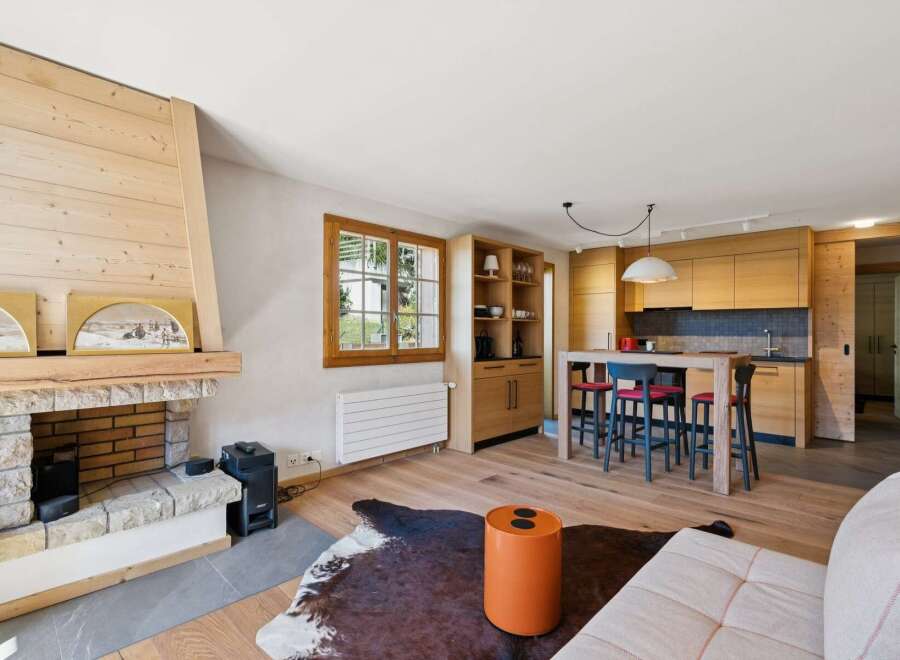 Experience modern alpine living in this beautifully appointed open-plan space, featuring a cozy stone fireplace and a sleek, wood-paneled kitchen.