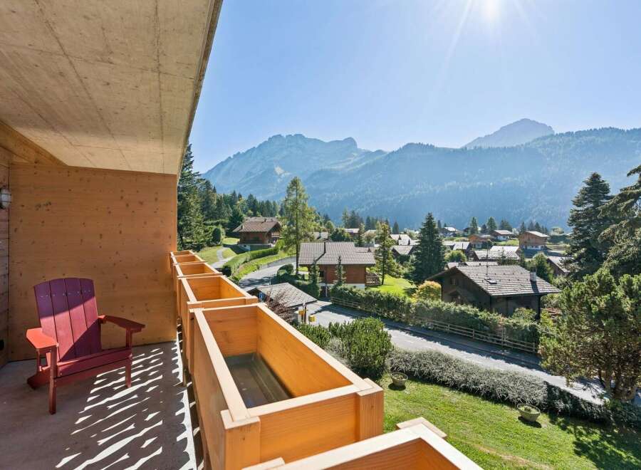 Enjoy breathtaking mountain views from this charming balcony, complete with a comfortable red Adirondack chair and wooden planter boxes.