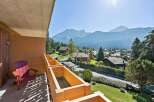 Enjoy breathtaking mountain views from this charming balcony, complete with a comfortable red Adirondack chair and wooden planter boxes.