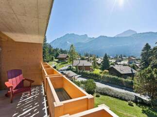 Enjoy breathtaking mountain views from this charming balcony, complete with a comfortable red Adirondack chair and wooden planter boxes.