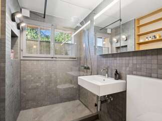 This modern bathroom features a sleek design with grey tiled walls and floors, complemented by a floating white sink and a glass-enclosed shower.