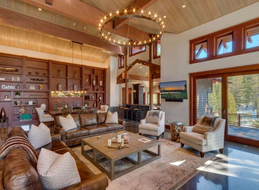 Experience luxurious mountain living in this stunning great room, featuring a grand circular chandelier and soaring wood-beamed ceilings.