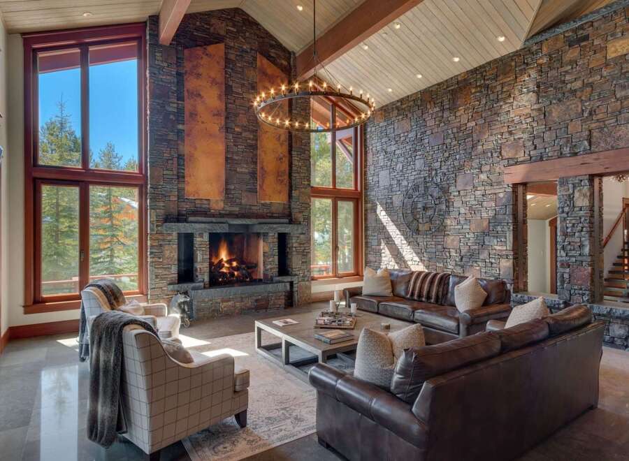 Experience luxury mountain living in this stunning great room, featuring a soaring stone fireplace and expansive windows that frame breathtaking forest views.