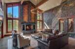 Experience luxury mountain living in this stunning great room, featuring a soaring stone fireplace and expansive windows that frame breathtaking forest views.