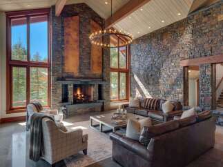 Experience luxury mountain living in this stunning great room, featuring a soaring stone fireplace and expansive windows that frame breathtaking forest views.