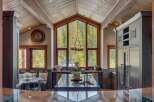Experience luxury mountain living in this stunning kitchen featuring a grand vaulted ceiling with exposed beams and a massive A-frame window showcasing breathtaking forest views.
