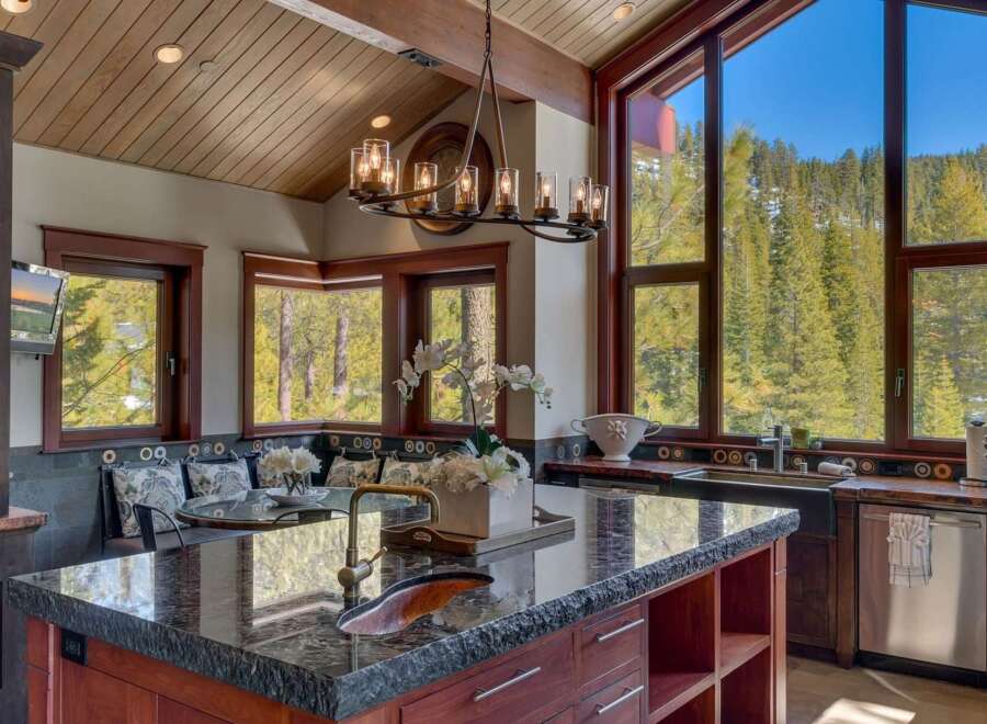 Experience luxury mountain living in this stunning kitchen, featuring a large granite island with a copper sink and a beautiful chandelier.