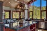 Experience luxury mountain living in this stunning kitchen, featuring a large granite island with a copper sink and a beautiful chandelier.