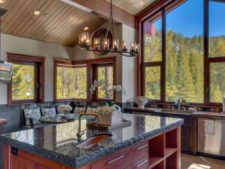 Experience luxury mountain living in this stunning kitchen, featuring a large granite island with a copper sink and a beautiful chandelier.
