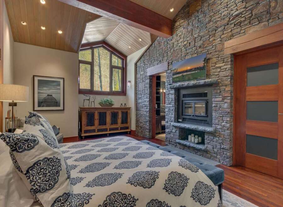 Experience rustic luxury in this stunning bedroom featuring a dramatic vaulted wood-paneled ceiling and a striking floor-to-ceiling stone fireplace.
