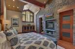 Experience rustic luxury in this stunning bedroom featuring a dramatic vaulted wood-paneled ceiling and a striking floor-to-ceiling stone fireplace.