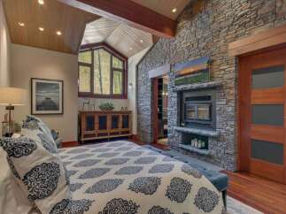 Experience rustic luxury in this stunning bedroom featuring a dramatic vaulted wood-paneled ceiling and a striking floor-to-ceiling stone fireplace.