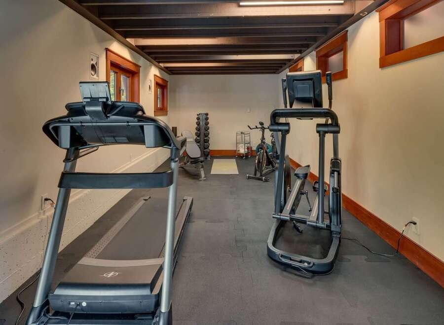 This home gym features a treadmill and elliptical for cardio workouts, alongside a weight bench and rack for strength training.