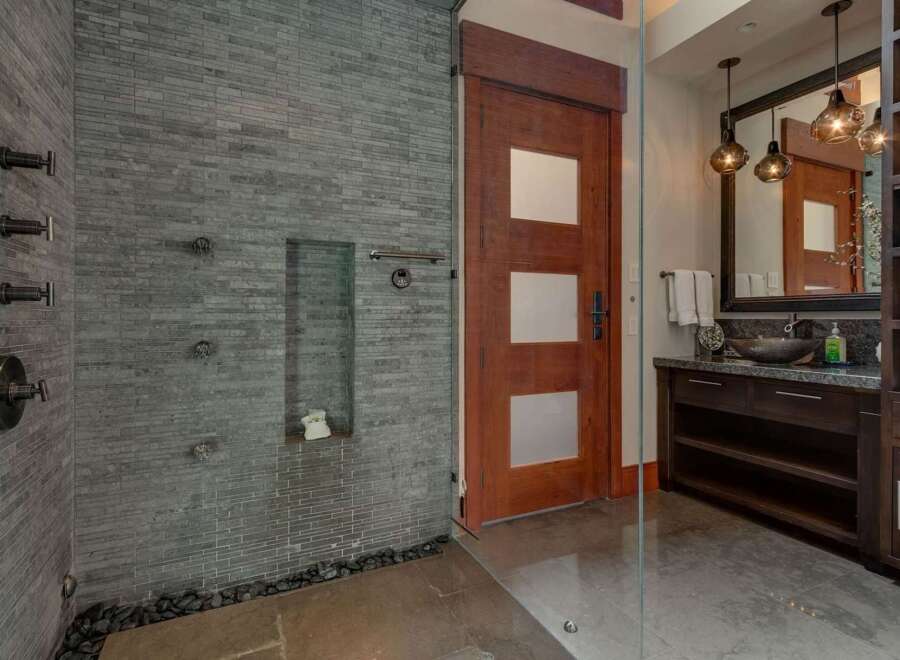 Experience luxury in this modern bathroom featuring a spacious walk-in shower with multiple showerheads and sleek stone tilework.